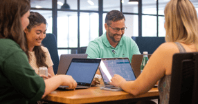 The Direct Development team is pictured sitting at a table with laptops, hard at work providing higher education marketing services