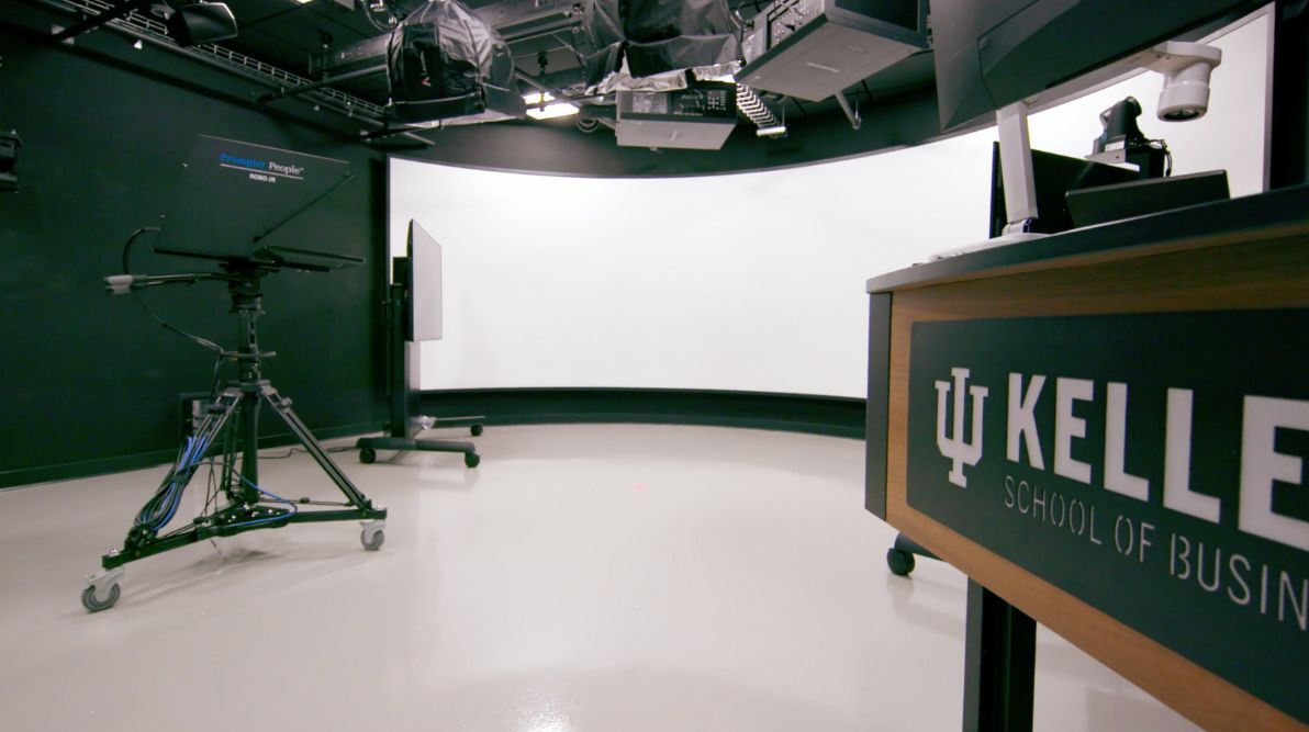 A recording studio with a camera on a tripod, a curved white screen, and a desk labeled